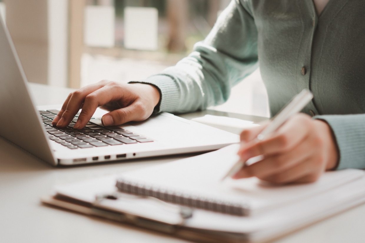 Business women work on computers and write on notepad with pen to onboard clients