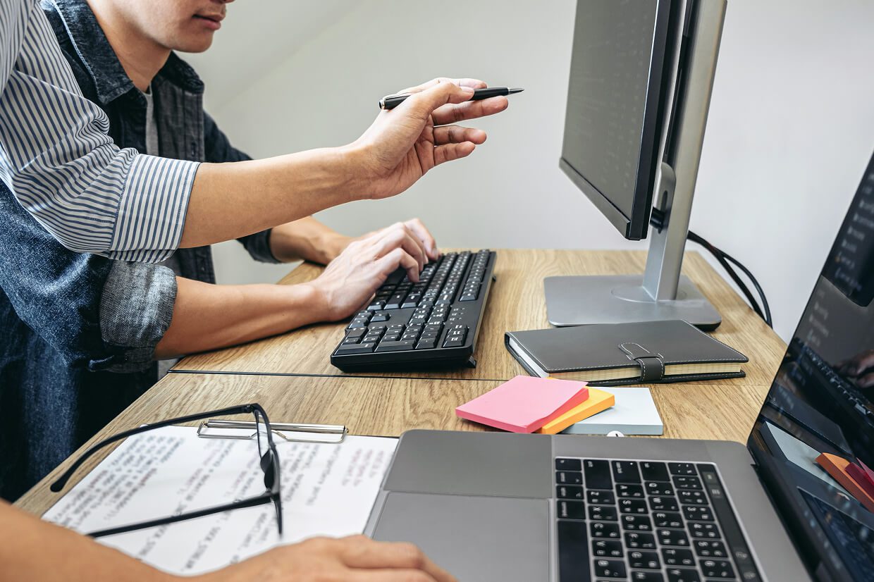 Monitor, hand on keyboard and someone pointing to screen