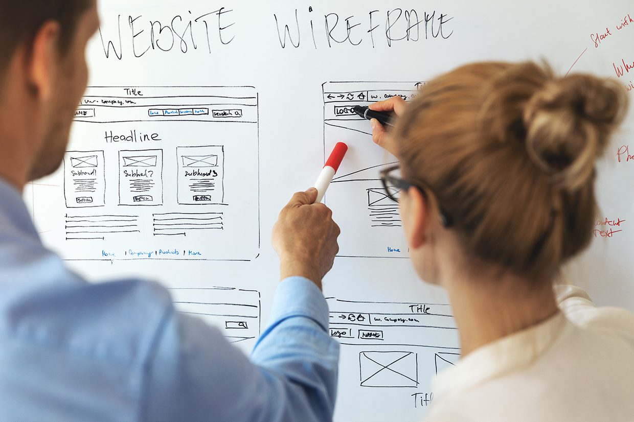 Woman and man pointing to white board labeled Website Wireframe